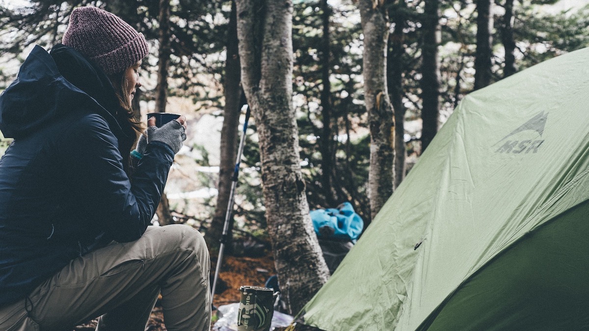 Girl sipping drink in the woods next to her tent