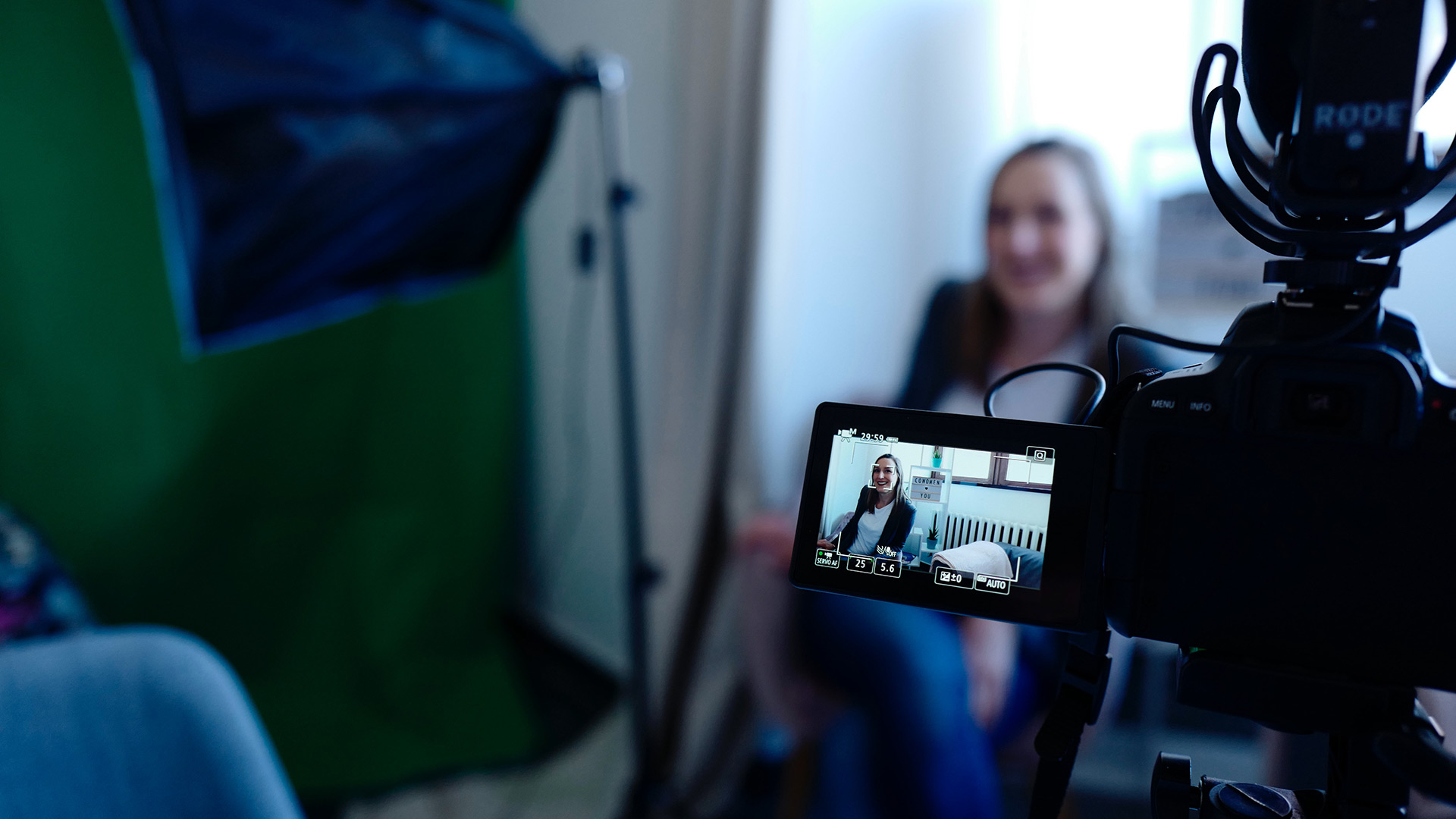 Picture of a woman being filmed from behind the video camera and monitor